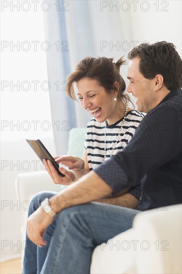 Couple sitting on sofa looking at digital tablet.