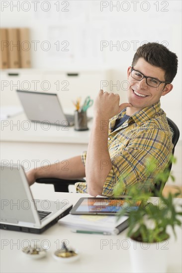 Young man sitting in front of desk and smiling.