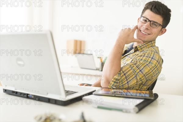 Young man sitting in front of desk and smiling.