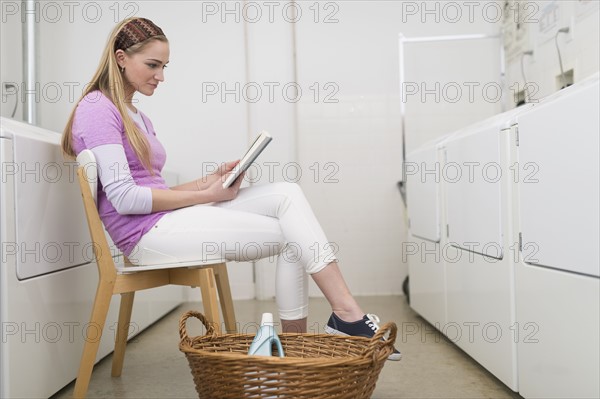 Woman reading book in laundromat.