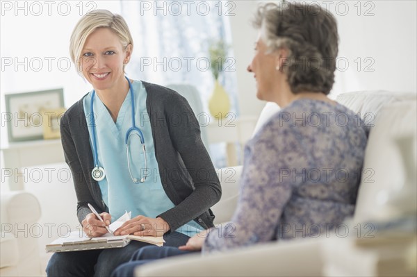 Nurse and mature woman sitting on sofa.