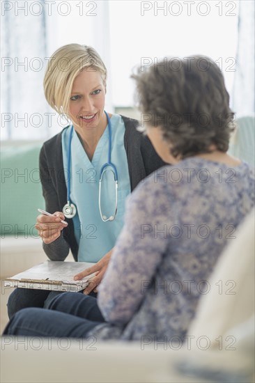 Nurse and mature woman sitting on sofa.