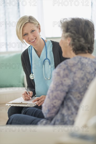 Nurse and mature woman sitting on sofa.