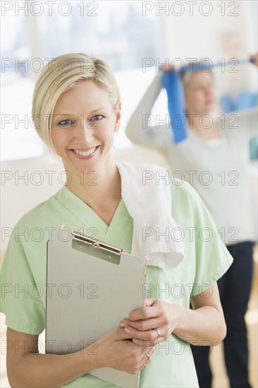 Portrait of personal trainer, mature woman exercising in background.