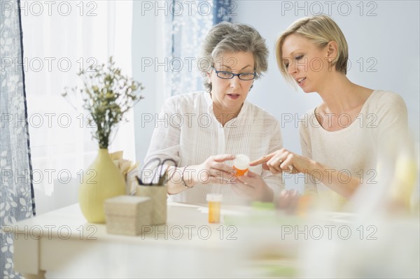 Nurse and mature woman reading labels on medicine bottle.