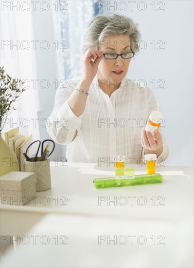 Mature woman reading labels on medicine bottle.