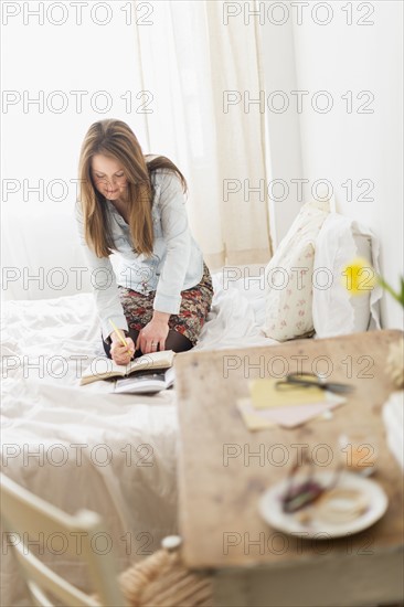 Woman kneeling on bed and writing diary.