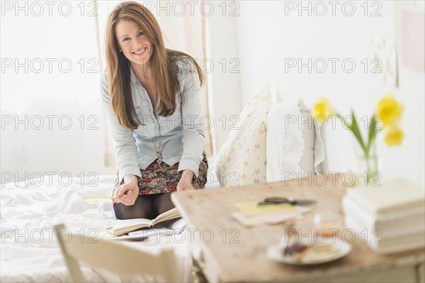 Woman kneeling on bed and writing diary.