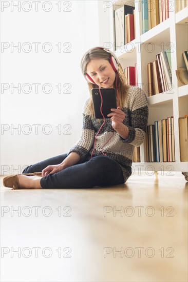 Young woman sitting on floor and listening to music on digital tablet.