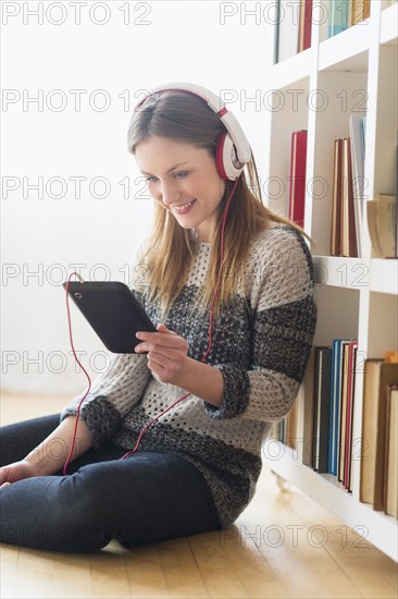 Young woman sitting on floor and listening to music on digital tablet.