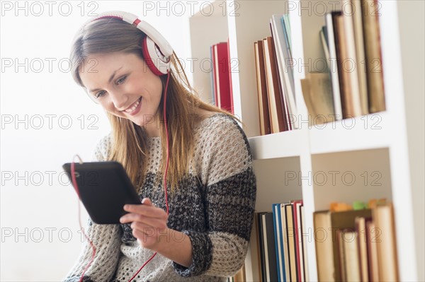 Young woman sitting on floor and listening to music on digital tablet.