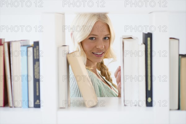 Portrait of young woman peeking through bookshelf.
Photo : Jamie Grill