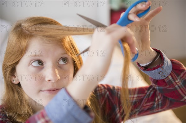 Portrait of girl (12-13) cutting her hair.
Photo : Jamie Grill