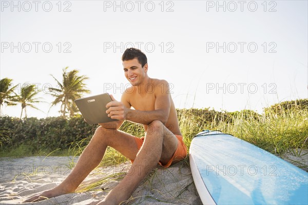 Young man sitting on beach with surfboard and digital tablet. Jupiter, Florida, USA.
Photo : Daniel Grill