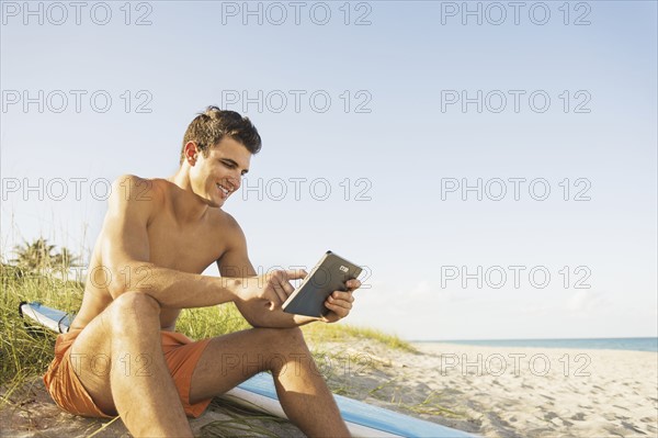 Young man sitting on beach with surfboard and digital tablet. Jupiter, Florida, USA.
Photo : Daniel Grill