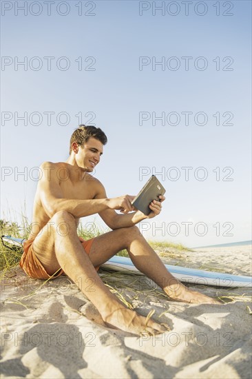 Young man sitting on beach with surfboard and digital tablet. Jupiter, Florida, USA.
Photo : Daniel Grill