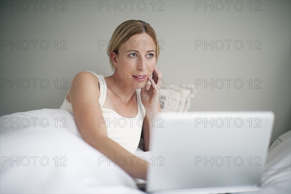 Woman with laptop contemplating in bed.
Photo : Mark de Leeuw