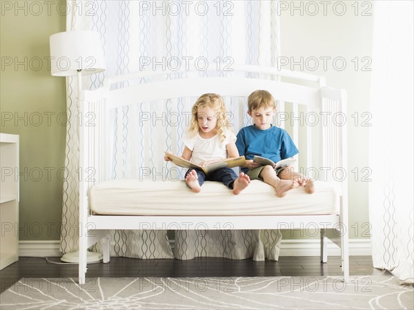 Girls (6-7) and boy (8-9) sitting on sofa and reading book.
Photo : Jessica Peterson