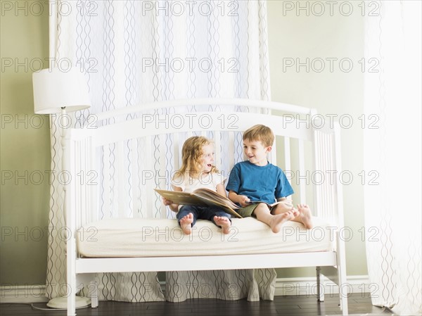 Girls (6-7) and boy (8-9) sitting on sofa and reading book.
Photo : Jessica Peterson