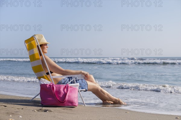 Woman sitting on deckchair on beach.