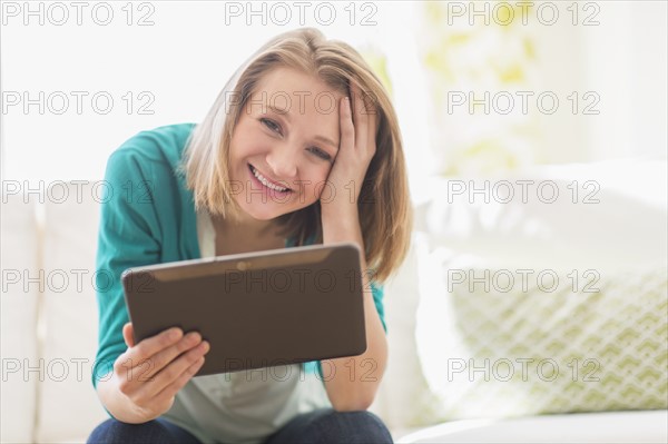 Portrait of woman on sofa holding digital tablet.