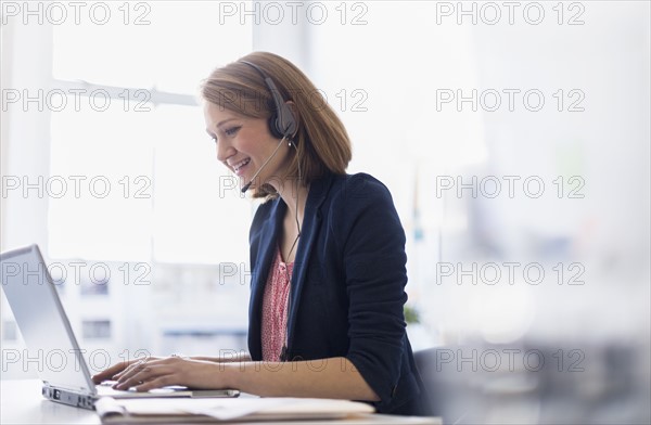 Young office worker talking on headset and typing.