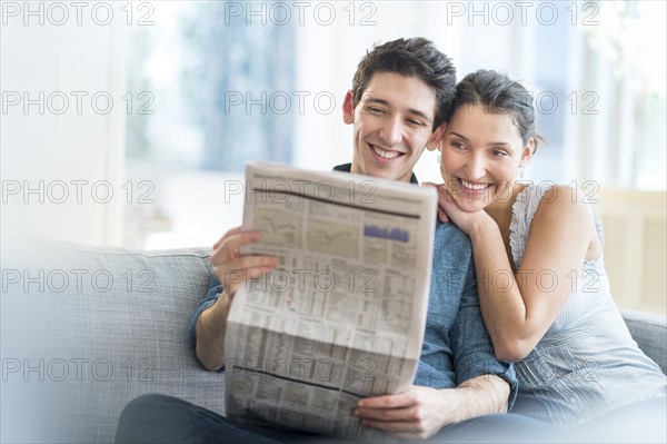 Couple reading newspaper on sofa.