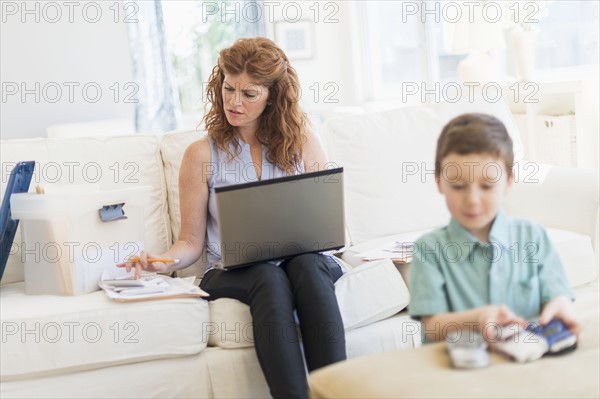 Mother using laptop, son (6-7) playing with toy cars.
