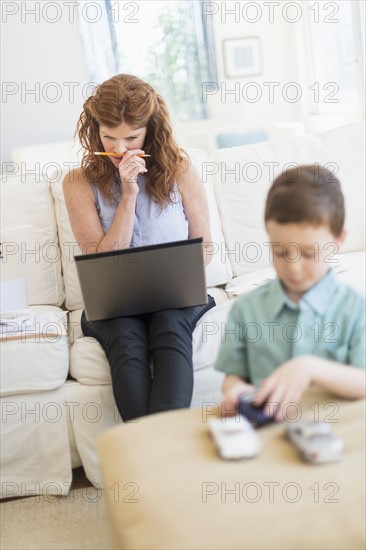 Mother using laptop, son (6-7) playing with toy cars.