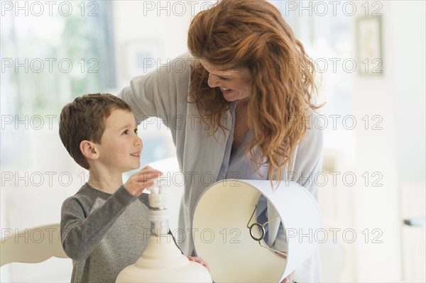 son (6-7) and mother changing lightbulb in table lamp.