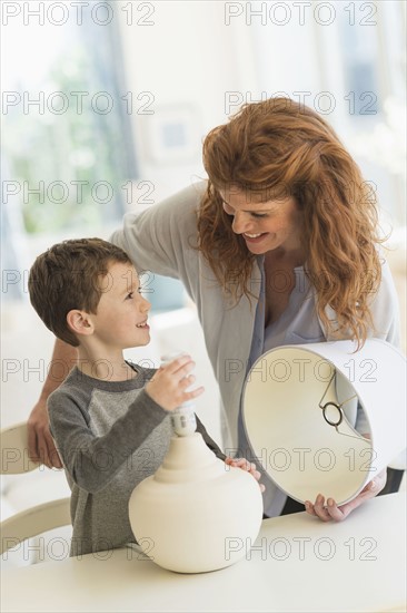 son (6-7) and mother changing lightbulb in table lamp.