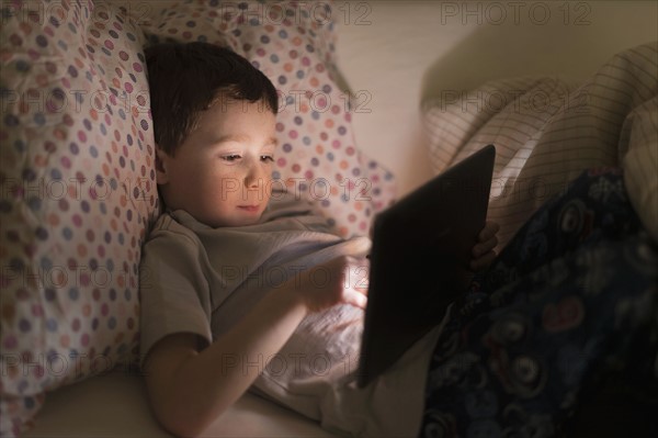 boy (6-7) using digital tablet in bed.