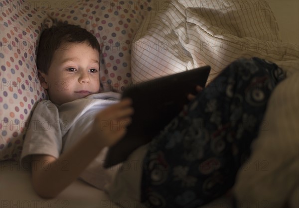 boy (6-7) using digital tablet in bed.