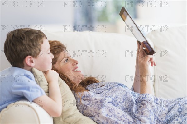 Mother and son (6-7) lying on sofa using digital tablet.