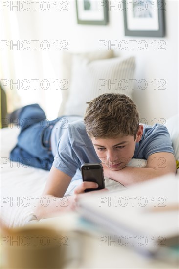 Teenage boy (16-17) lying on bed and text messaging.
