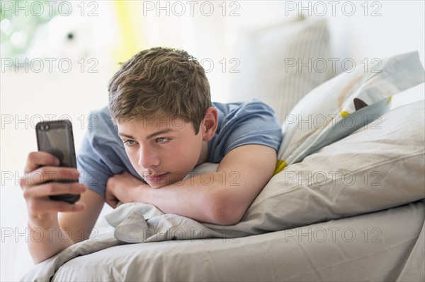 Teenage boy (16-17) lying on bed and text messaging.