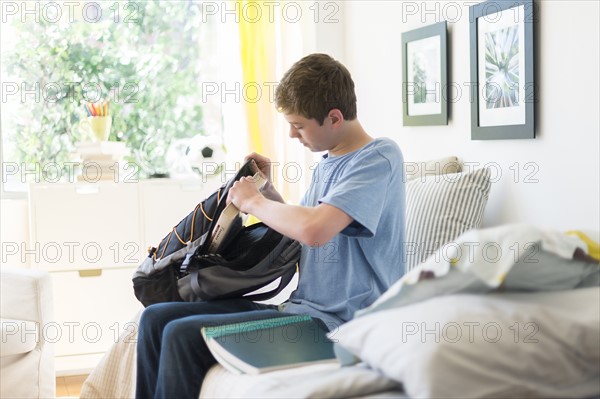 Teenage boy (16-17) packing books into backpack.