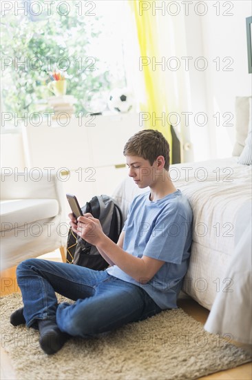 Teenage boy (16-17) using digital tablet in bedroom.