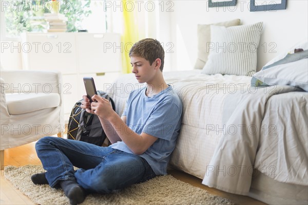 Teenage boy (16-17) using digital tablet in bedroom.