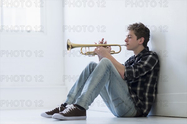 Teenage boy (16-17) playing trumpet in hallway.