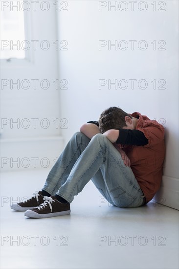 Teenage boy (16-17) sitting in hallway.