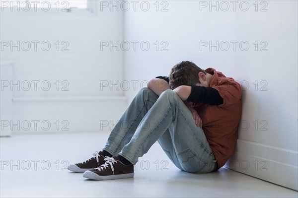 Teenage boy (16-17) sitting in hallway.