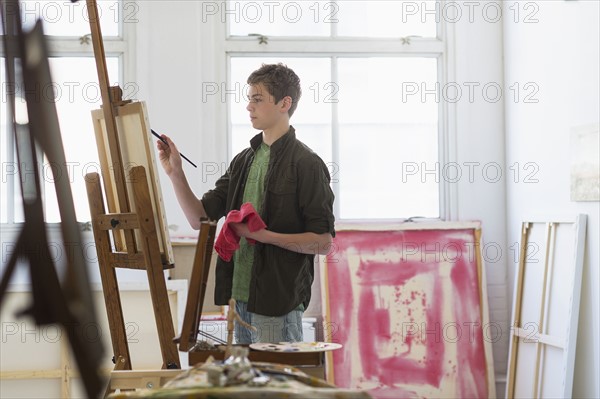 Teenage boy (16-17) painting picture.