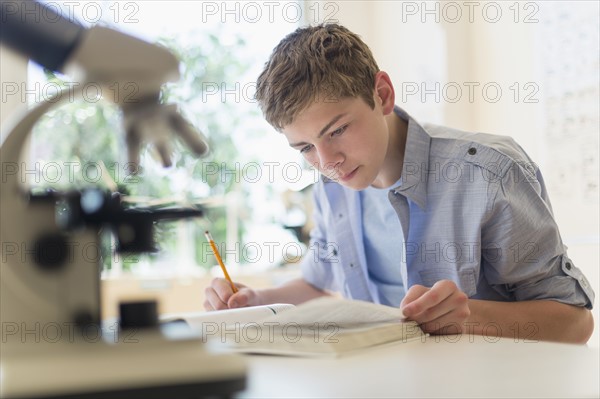 Teenage boy (16-17) reading book in laboratory.