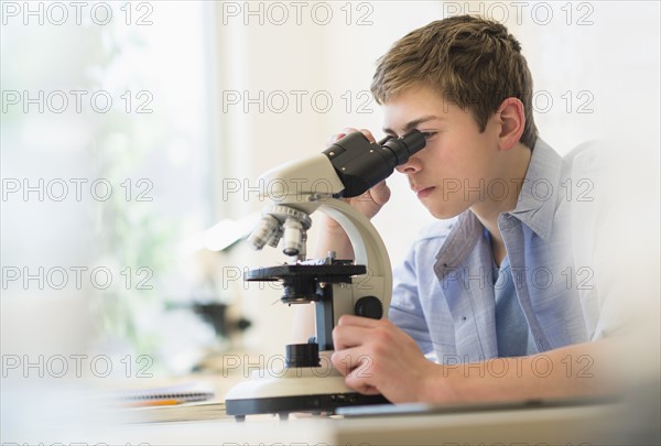 Teenage boy (16-17) looking through microscope.