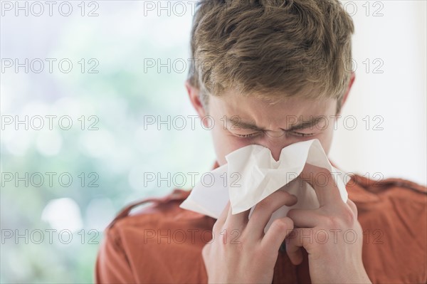 Teenage boy (16-17) blowing nose.