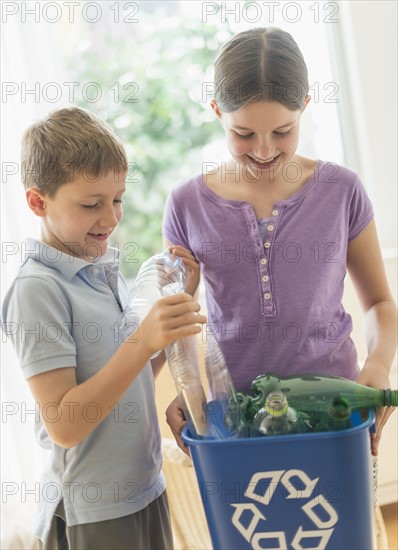 Boy and girl (8-9, 10-11) placing bottles in garbage bin.