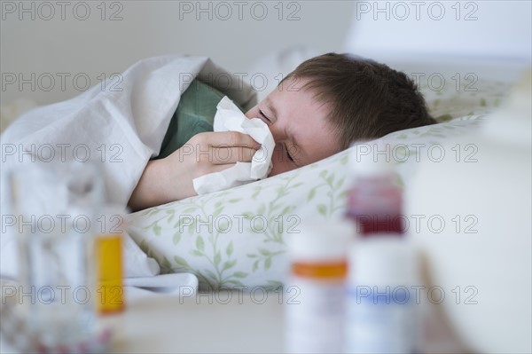 boy (8-9) lying in bed and blowing nose.