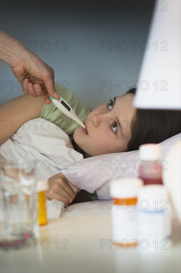 Sick girl (8-9) with thermometer in mouth.