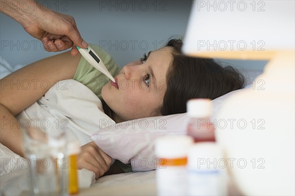 Sick girl (8-9) with thermometer in mouth.